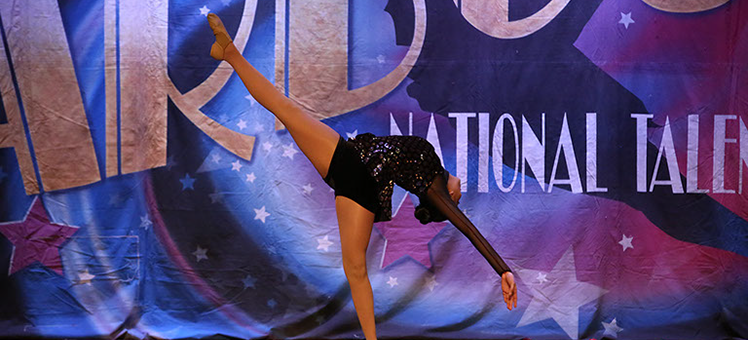 A girl onstage at Starbound National Talent Competition doing a layout. She is wearing a dark glittery costume. This is a jazz dance.