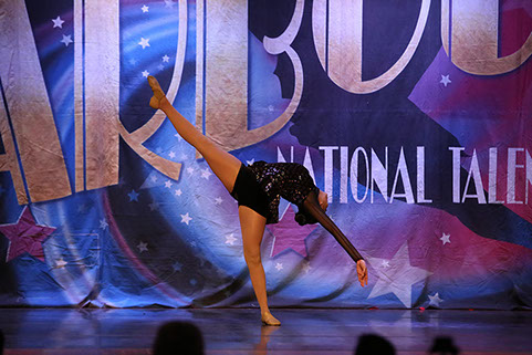 A girl onstage at Starbound National Talent Competition doing a layout. She is wearing a dark glittery costume. This is a jazz dance.