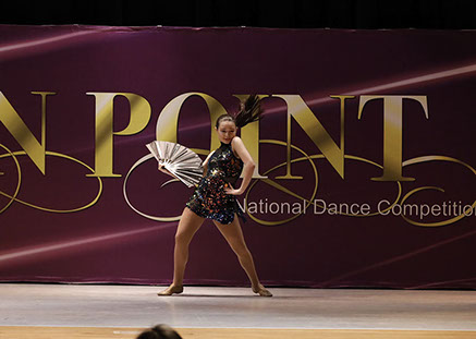 A girl on stage at Starbound National Dance Competition with a dark glittery costume and a fan. This picture is from a jazz dance.