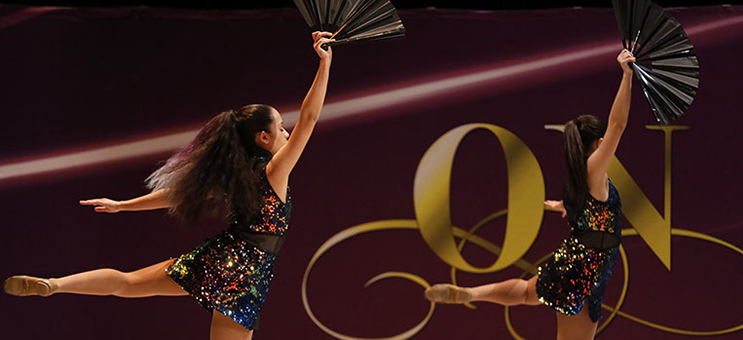 Two girls on stage at On Point Dance Competition in "oilslick" costumes, holding fans and doing an attitude. This picture is from a jazz dance.