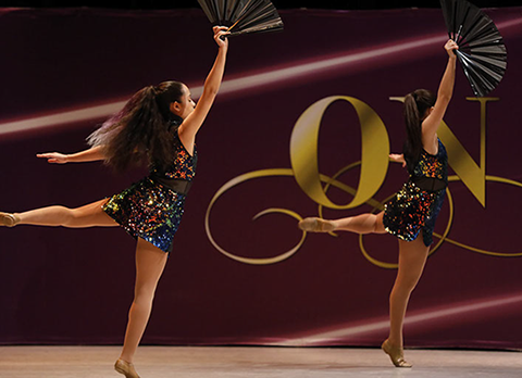Two girls on stage at On Point Dance Competition in "oilslick" costumes, holding fans and doing an attitude. This picture is from a jazz dance.