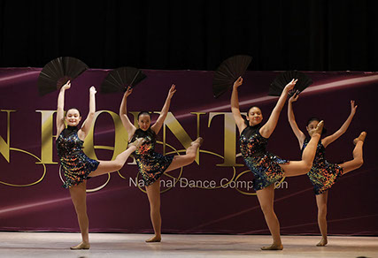 Four girls on stage at OnPoint Dance Competition in "oilslick" costumes and holding fans, doing an attitude. This picture is from a jazz dance.