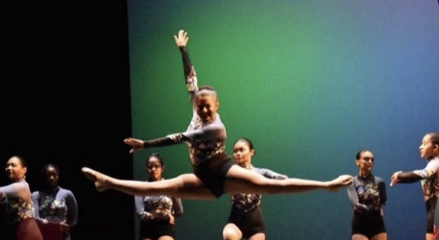 Various girls on stage at Kean University in purple and black costume. One girl is midair doing a perfect leap.